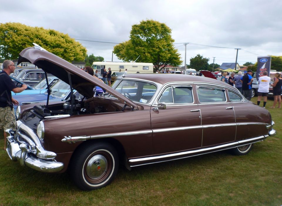Brown 1950s sedan with hood open at a car show.
