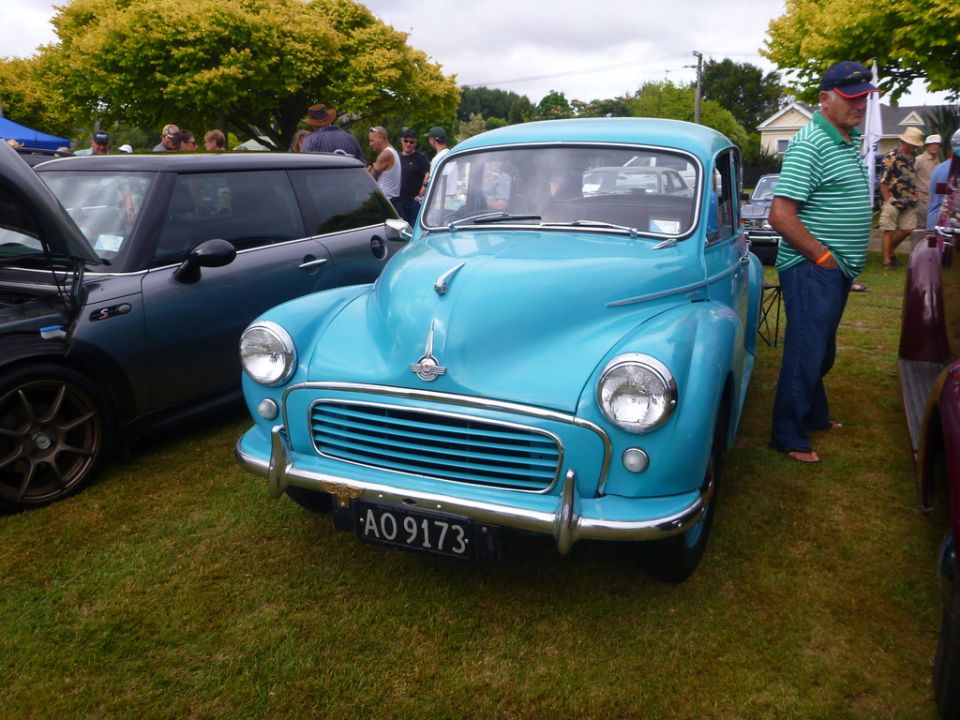 Blue classic car with chrome grille and bumper, parked on grass next to a dark gray Mini Cooper.