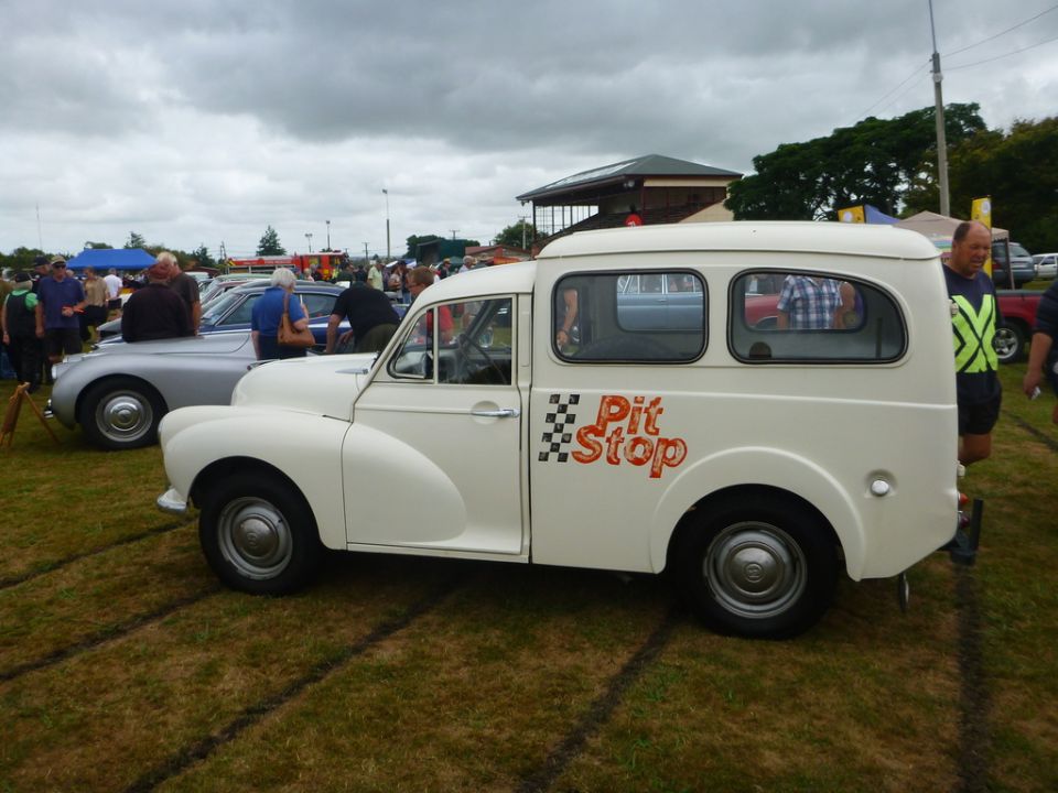 White vintage van with "Pit Stop" text parked on grass at an outdoor event.