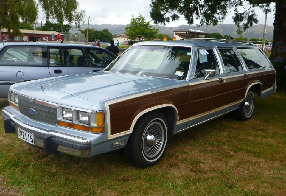 Light blue station wagon with wood paneling, parked outside with a "FOR SALE" sign.