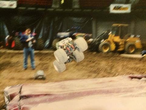 1989 Ford Bronco - A monster truck is captured mid-air during a competition, with a yellow loader visible in the background.