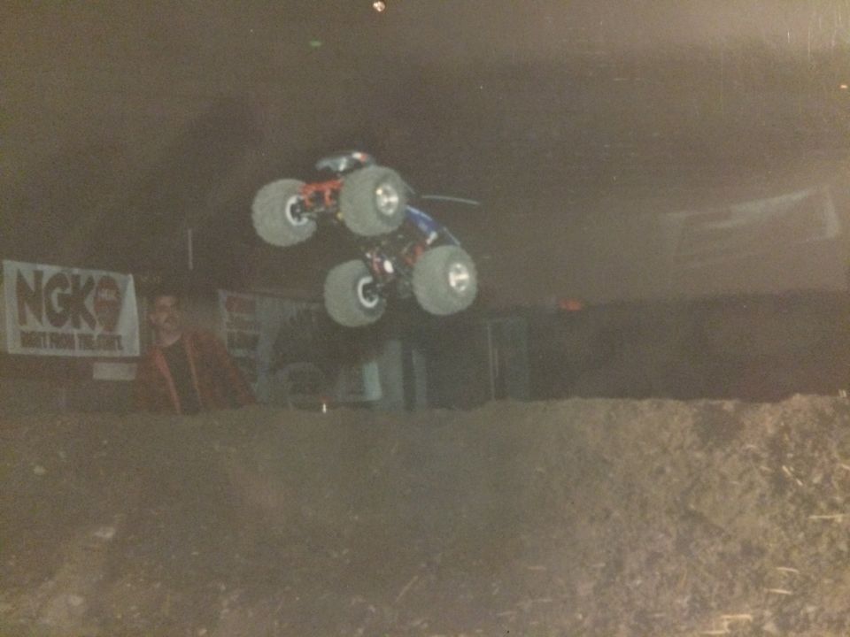Monster truck airborne over dirt track, NGK banner visible