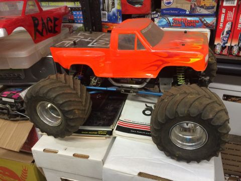 1989 Ford Bronco - A custom-built RC monster truck with an orange Ford Bronco-style body, featuring flame graphics and large, knobby tires, sits on a stack of…