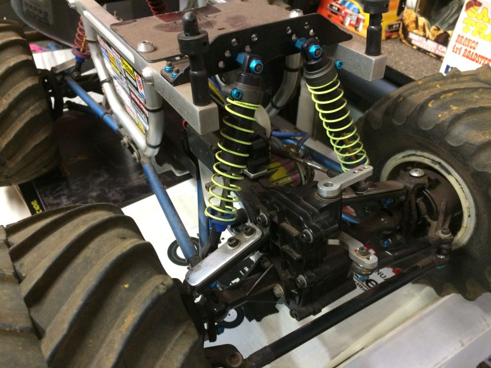 Remote-controlled monster truck suspension and drivetrain with large tires and yellow shocks.