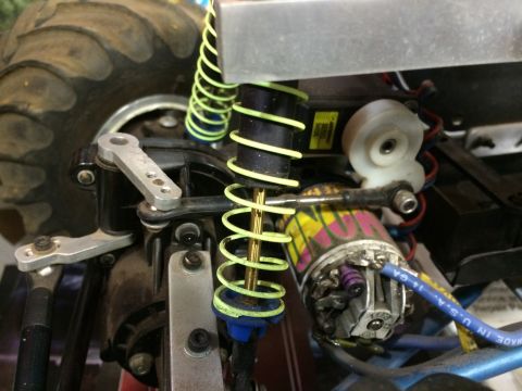 1989 Ford Bronco - Close-up view of the suspension and steering components of an RC car, featuring a large tire, a yellow-wound shock absorber, and a brushed…