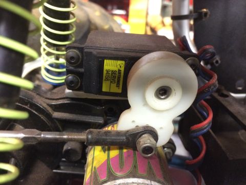 1989 Ford Bronco - A close-up view of a servo motor with a white servo horn attached to a linkage rod. The servo has a yellow label that reads "AIRTRONICS SER…