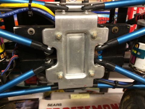 1989 Ford Bronco - A close-up view of the suspension components of a custom RC car, featuring blue metal suspension arms and a silver aluminum chassis brace.