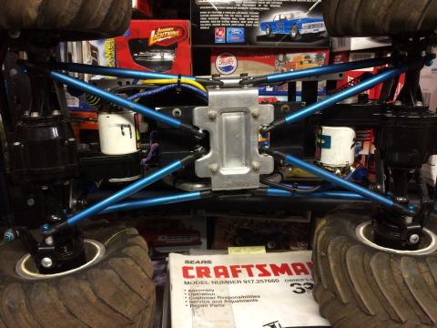 1989 Ford Bronco - The underside of a modified RC monster truck is shown, featuring bright blue suspension linkages and large, knobby tires. A Sears Craftsman…