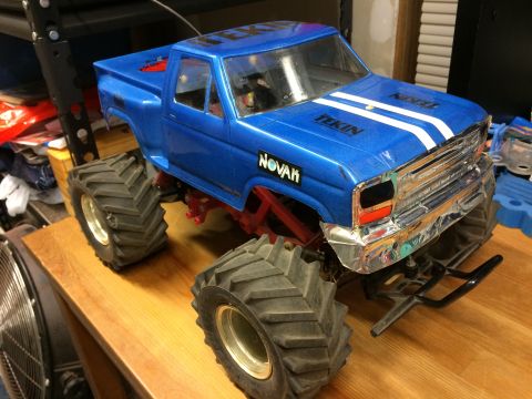 1989 Ford Bronco - A blue remote-controlled monster truck with large tires and chrome accents sits on a wooden surface. White stripes and black lettering are…