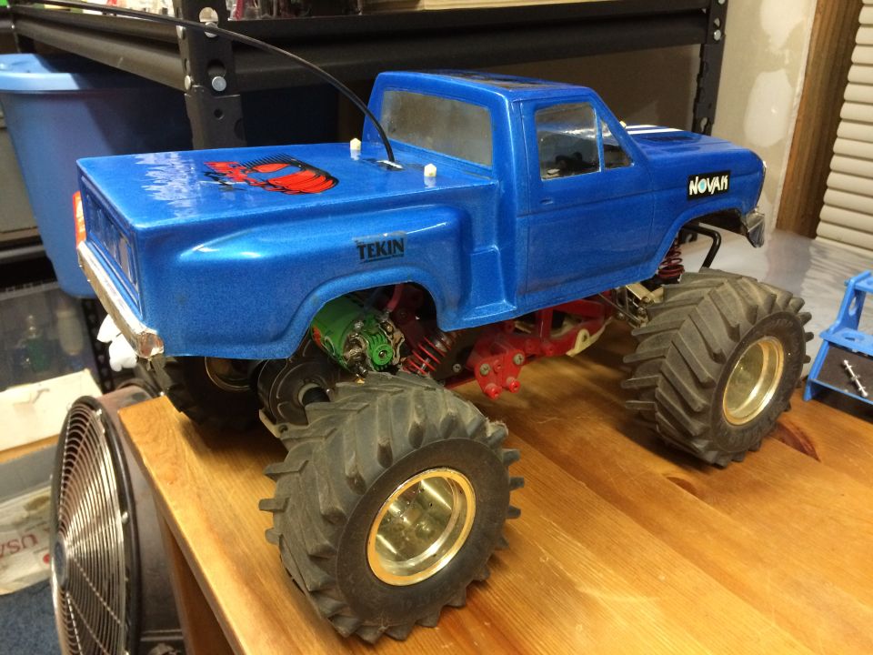 Blue RC monster truck with large tires and red decal on bed.