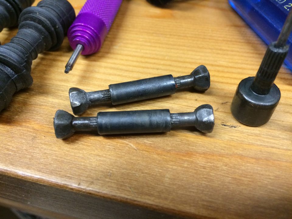 Two black metal drive shafts with splined and flared ends on a wooden surface.