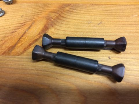1989 Ford Bronco - Two black metal shafts with splined ends and flared conical tips are laid diagonally on a wooden surface.