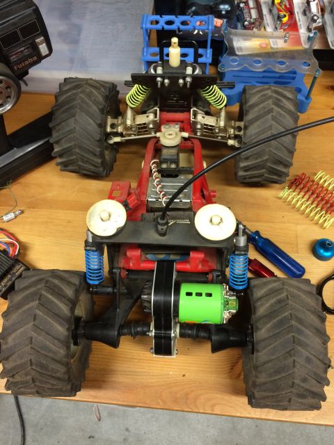1989 Ford Bronco - A top-down view of a red and black remote-controlled monster truck chassis with large tires, a green motor, and yellow and blue suspension…
