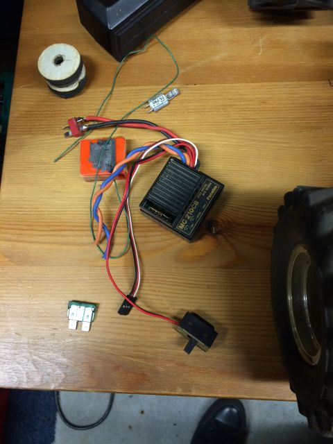 1989 Ford Bronco - A collection of electronic components, including a Futaba MC-210CB speed controller, a fuse, a switch, and various wires, are laid out on a…