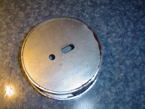 1986 Ford Bronco - A round metal part with two holes, one circular and one slotted, is shown on a speckled blue countertop.