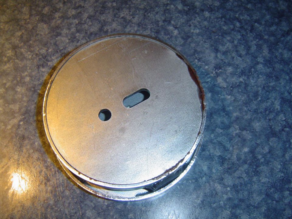 Round metal part with two holes on a speckled blue surface.