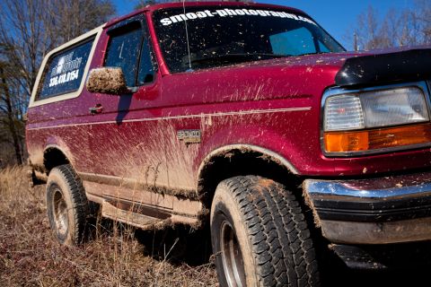 1995 Ford Bronco - A muddy red 1995 Ford Bronco is shown from a 3/4 front angle, indicating it has been used off-road.