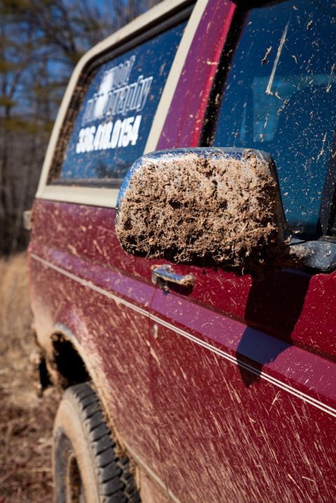 1995 Ford Bronco - This red SUV is heavily covered in mud, suggesting it has been off-roading. A phone number is visible on the rear window.