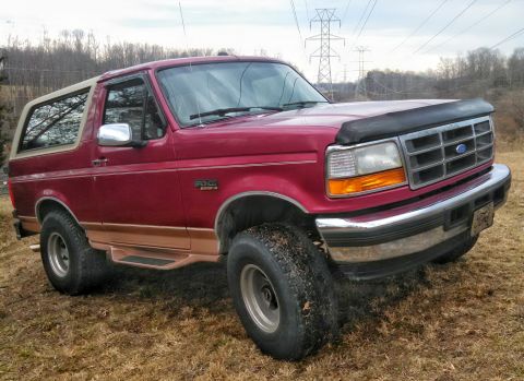 1995 Ford Bronco - This lifted Ford Bronco has a two-tone paint scheme and is parked outdoors on a grassy field.