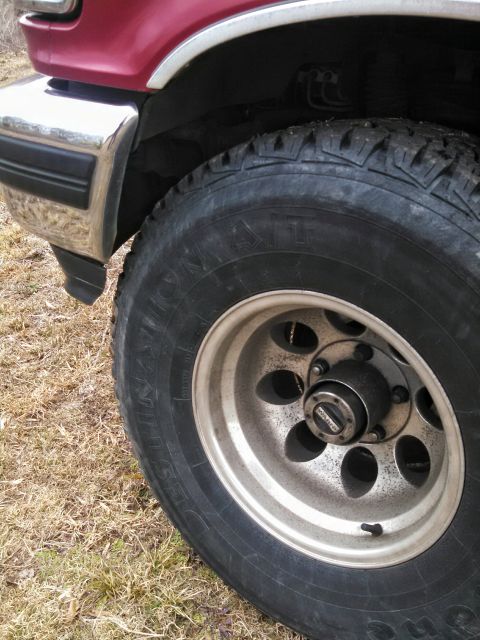 1995 Ford Bronco - Close-up of a red SUV's front fender and wheel, an off-road tire and chrome bumper detail.