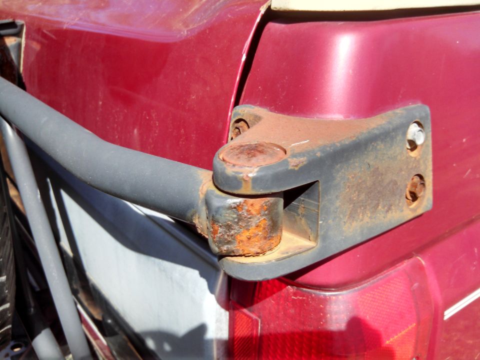 rusted trailer hitch mount attached to the rear corner of a red vehicle