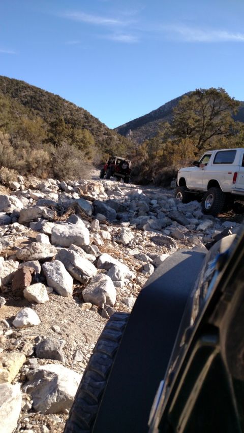 1979 Ford Bronco - Two off-road vehicles navigate a challenging, rocky mountain path under a clear blue sky. The white SUV in the foreground resembles a 1979…