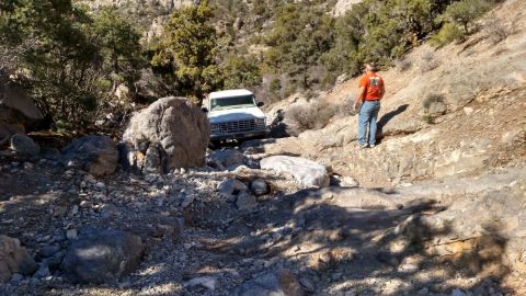 1979 Ford Bronco - A white SUV is carefully driven over a rough, rocky terrain in a mountainous area.