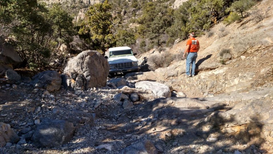 White SUV navigating a rocky, off-road trail with a person standing on the side