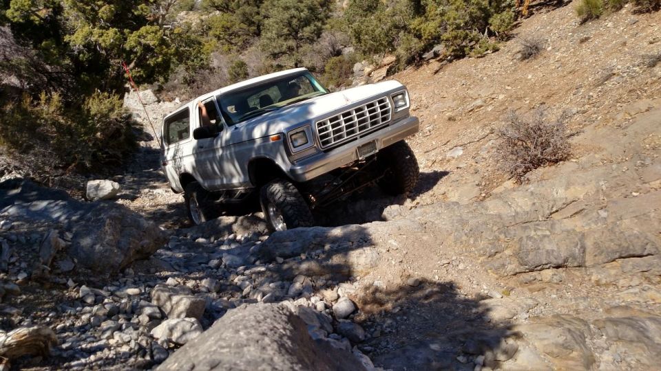 White 1978 Ford Bronco driving over rocks on a dry, mountainous trail