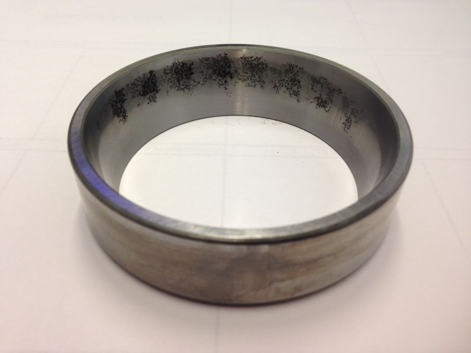 Close-up of a metal bearing race with dark pitting and wear marks on the inner surface