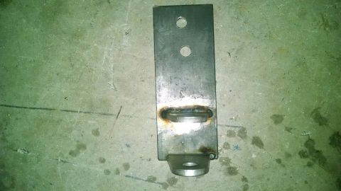 1979 Ford Bronco - A metal bracket with welded loops and drilled holes sits on a stained concrete surface.