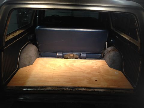 1979 Ford Bronco - The interior cargo area of a vehicle shows a wooden floor and a blue bench seat, with visible wheel wells.