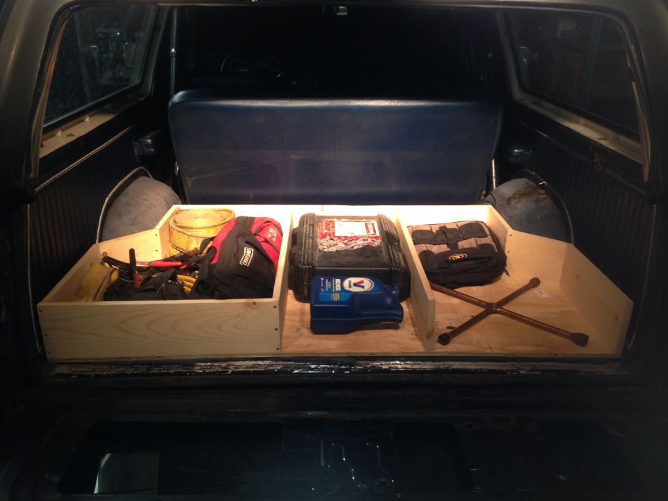 Custom wooden storage box with tools, bags, and a jack in the cargo area of an older SUV