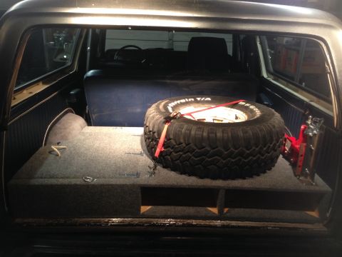 1979 Ford Bronco - The interior cargo area of a vehicle shows a spare tire and jack, with custom storage.