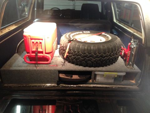 1979 Ford Bronco - The interior storage area of a vehicle contains a red cooler and a spare tire mounted on a custom storage box.
