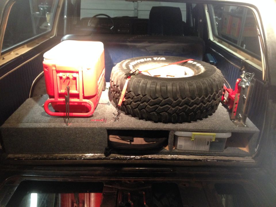 Storage box with red cooler and spare tire inside a vehicle interior