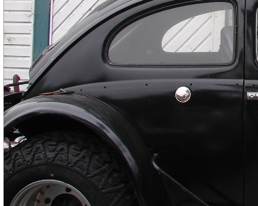 Side view of a black vintage car with a round chrome fuel cap and a distinctive window shape