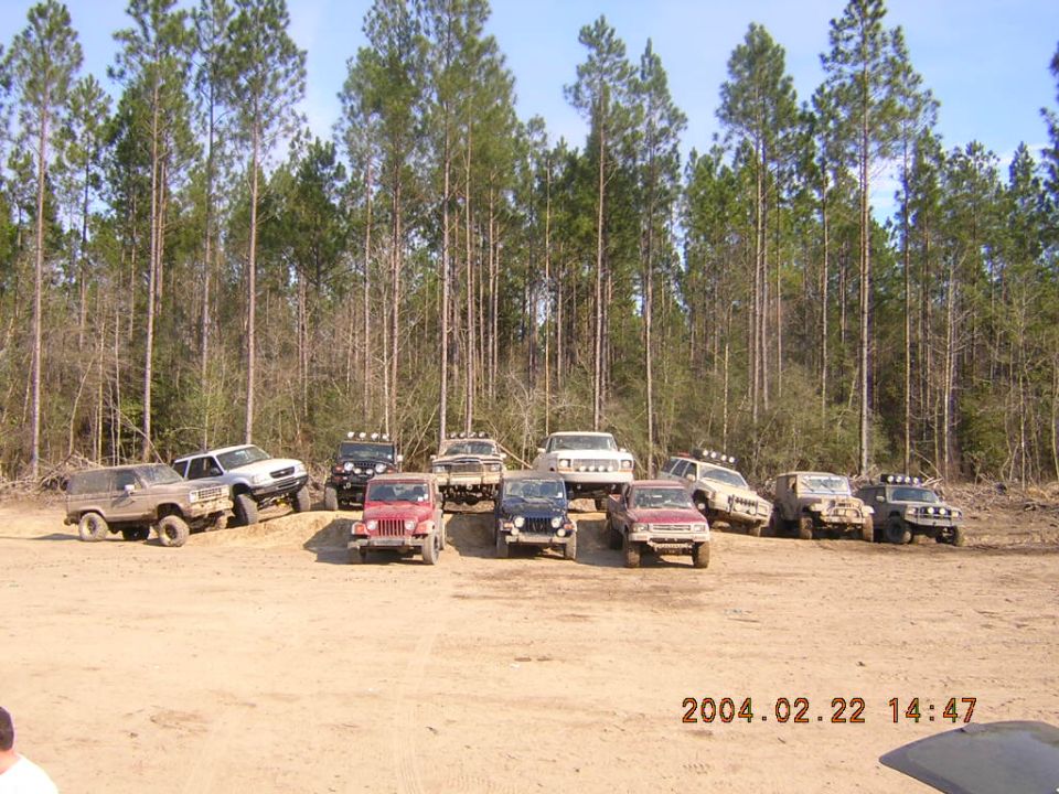 Several off-road SUVs and Jeeps parked on a dirt lot with trees in the background