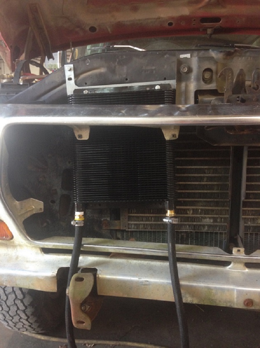 Front end of a vehicle with a new transmission cooler installed in front of the radiator. Hoses run from the cooler
