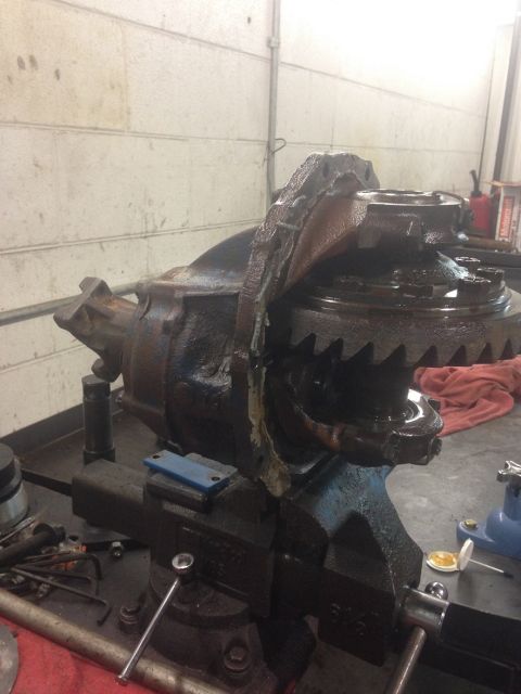 1978 Ford Bronco - A severely damaged differential assembly is clamped in a vise on a workbench, showing broken gears and casing.