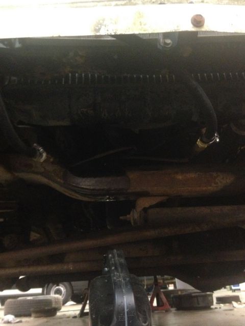 1978 Ford Bronco - Underside view of vehicle components, including suspension and hoses, with an oil drain pan in the foreground.