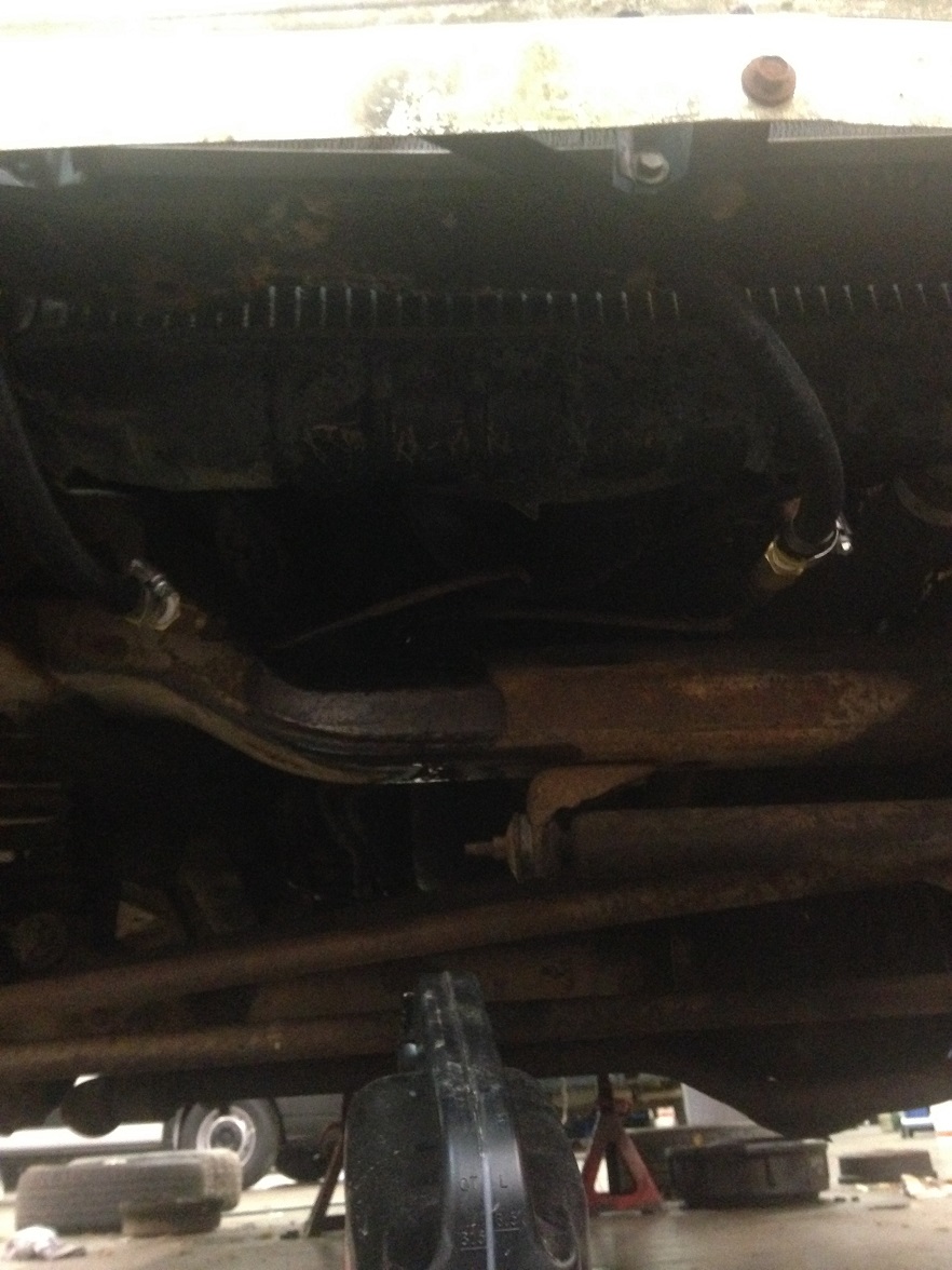 Underside view of vehicle showing suspension components and hoses. A black oil drain pan is visible