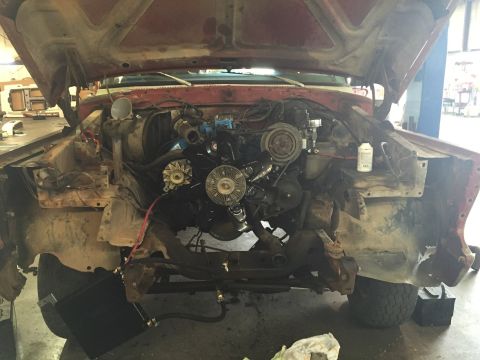 1978 Ford Bronco - The engine bay of a red vehicle is exposed with the hood up, revealing the engine and front suspension components.