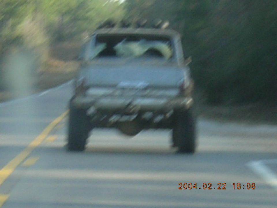 Rear view of lifted SUV with roof rack, driving on a road