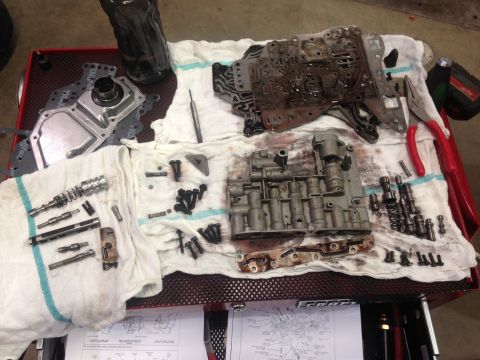 1978 Ford Bronco - Various transmission parts, including the valve body, are spread out on a red cart with diagrams visible below.