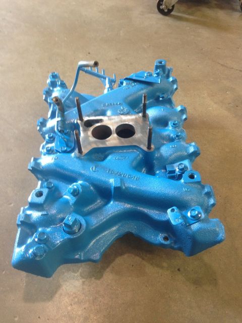 1978 Ford Bronco - A blue intake manifold sits on a concrete floor, showing its intricate casting and mounting points.