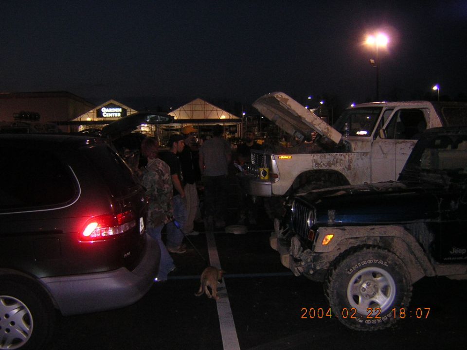 White SUV with hood open, dark SUV in foreground, people gathered