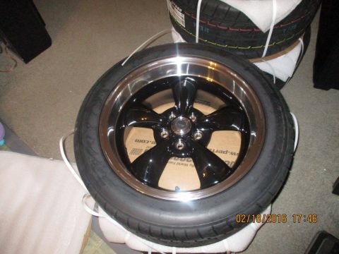 2004 Ford Crown Victoria - A black five-spoke wheel with a chrome lip is shown, with a tire mounted. Other tires are stacked in the background.