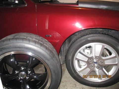 2004 Ford Crown Victoria - A red car fender displays an SVT badge next to two tires, one aftermarket and one OEM.