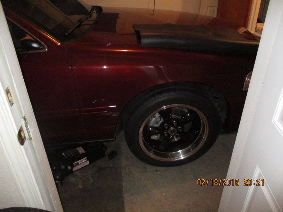 Maroon sedan in garage, jack under front wheel, aftermarket wheels, hood cover on